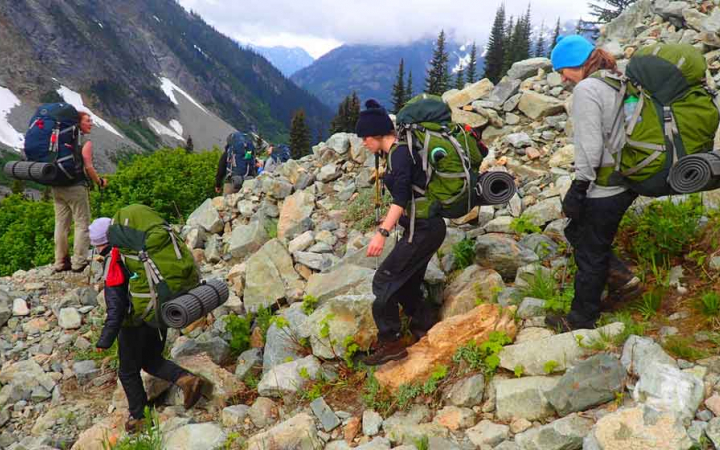 a group of teens crossing rocking terrain on outward bound backpacking expedition